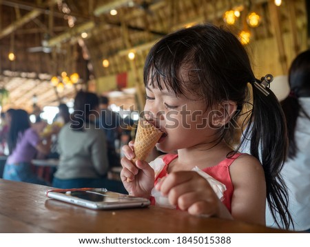 A girl wearing a hearing aid, Eating ice-cream and watch cartoons on the smart phone