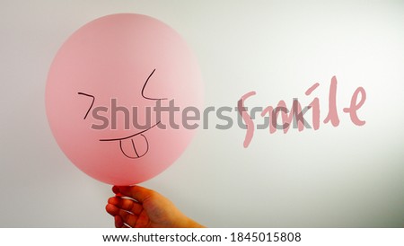 A pink balloon with a hand drawn picture of a happy, funny smiling face and smile text. Funky and warm background.