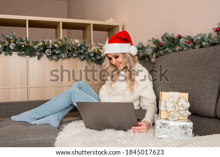 Christmas greetings online. a woman in a white sweater and red Santa hat uses a laptop to make video calls to friends, parents, and for online shopping.