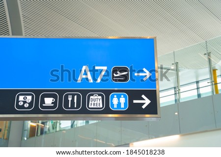 Shield with signs indicating airport amenities and public utilities, and arrow pointing to gate to board the plane for departure hangs on wall, close up