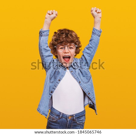 Excited schoolboy in casual wear standing with fists up on yellow background while screaming and celebrating achievement Royalty-Free Stock Photo #1845065746