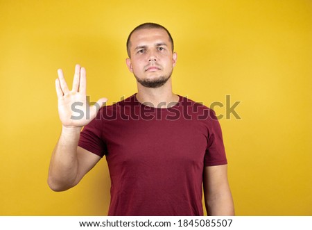 Russian man wearing basic red t-shirt over yellow insolated background doing hand symbol