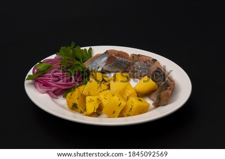 Russian appetizer on a black background in a white plate potatoes blue onions herring parsley