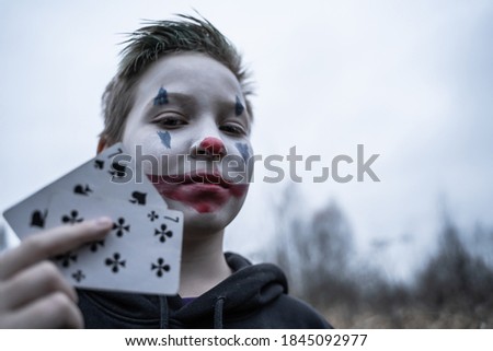 
A boy in a Joker costume. A teenager in makeup with cards in his hands.
