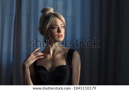 Close up studio portrait of a pretty blonde woman in black top, looking to the side. Blue eyes, young and tender. Horizontal photo.