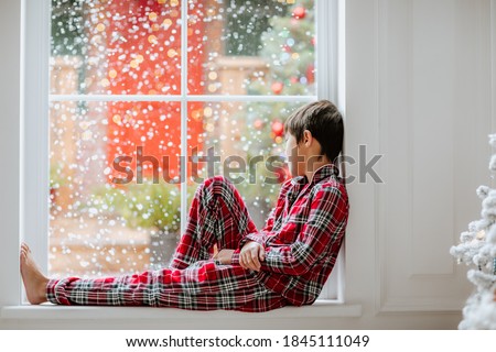 Young asian pretty boy in red pyjamas posing on the big window . High quality photo