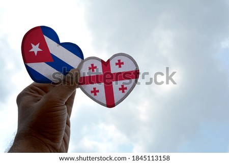Hand holds a heart Shape Cuba and Georgia flag, love between two countries
