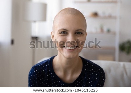 Head shot portrait smiling hairless woman making video call, looking at camera, sitting on couch at home, happy young female talking to doctor online, blogger recording video about oncology