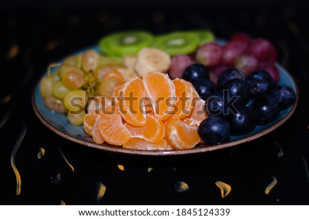 Fruits, grapes, tangerines, bananas, kiwi in a blue porcelain plate. black wooden floor, fruit plate
