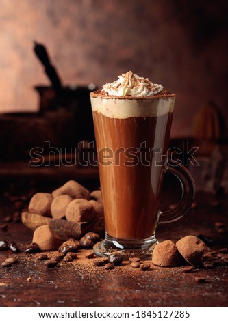 Truffles and glass of hot chocolate with whipped cream. Sweets and drink sprinkled with cocoa powder on an old brown table.