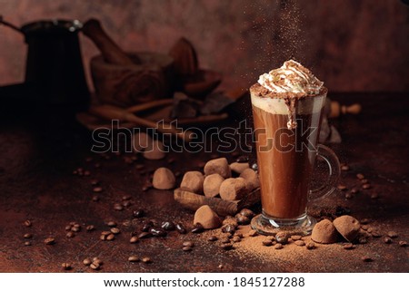Truffles and glass of hot chocolate with whipped cream. Sweets and drink sprinkled with cocoa powder on an old brown table.