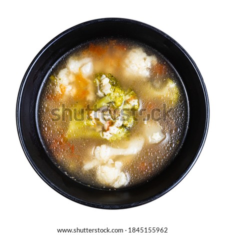top view of soup with stelline (italian pasta) and vegetables (cauliflower, broccoli, etc) in black bowl isolated on white background