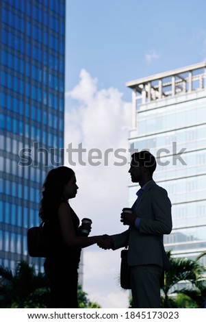 Silhouettes of young business people with coffee cups standing in the street and shaking hands