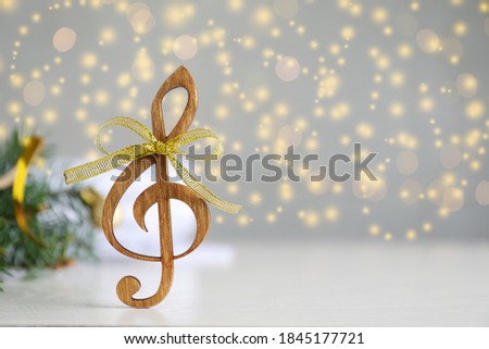 Wooden music note with golden bow on light grey table against blurred Christmas lights. Space for text
