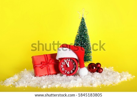 Alarm clock with Christmas decor on yellow background. New Year countdown