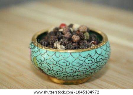 peppercorns in a ceramic plate on a wooden background. Space of your text.