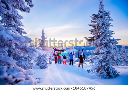 Group of happy team skiers and snowboarders stands on top of mountain winter forest. Sunrise blue sky.