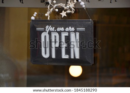 Sign "Yes, we are open" hanging on a glass door