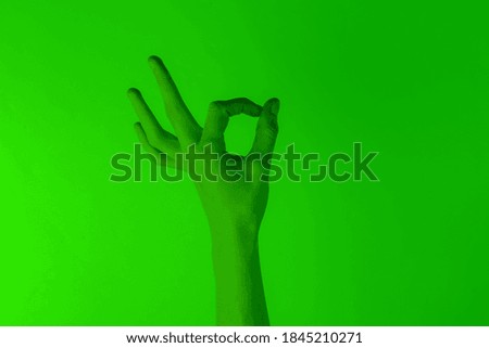 Female hand shows okay gesture in green neon light