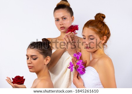 Attractive female models with hair pulled back, wrapped in white towels and holding flowers. Posing on a white background in the studio.