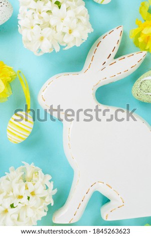 Easter scene with spring flowers, white rabbit and colored eggs close up, flat lay on blue background