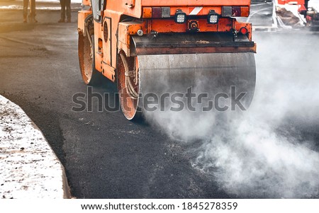 Vibration roller compactor lay new asphalt surface in wintertime. Road construction, asphalt roller press hot asphalt. Asphalt paving, steamroller machine  Royalty-Free Stock Photo #1845278359