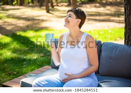 Happy pregnant woman sitting in summer Park