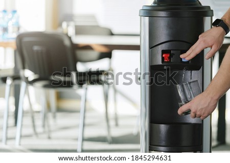 Water dispenser in the office, with hand filling a glass of water  Royalty-Free Stock Photo #1845294631