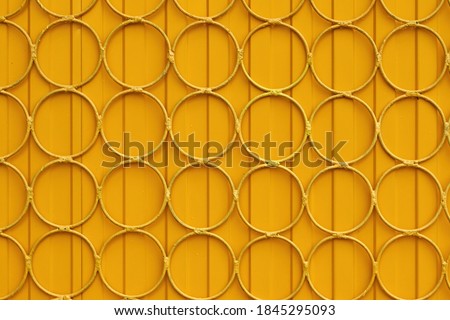 Close up yellow fence with metal grille in form of circles.