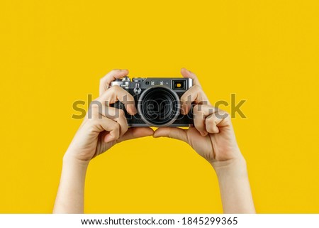 Digital camera held by 2 hands, yellow background