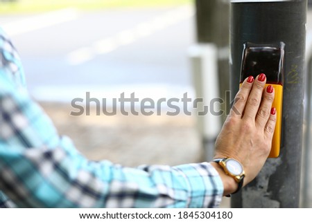 Close-up of woman pressing knob on metal pole. Inscription on smart screen please wait. Female with beautiful red manicure. Parking indicator. Lady in blue shirt