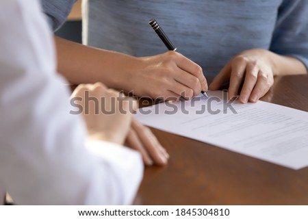 Last formality. Close up of young woman job applicant being hired on vacant place signing employment contract in presence of recruiter, female bank client putting signature under financial document