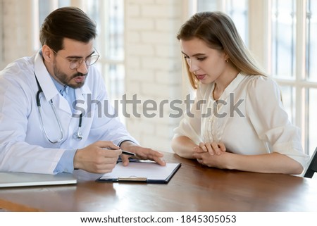Doc writing prescription. Capable qualified millennial male doctor attending physician gynecologist gp consulting young female patient at hospital cabinet, ordering medication, prescribing treatment Royalty-Free Stock Photo #1845305053