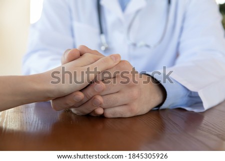We shall help you overcome health problem. Confident capable caring millennial male doctor talking with female patient holding her hand supporting comforting helping promising aid assistance, close up Royalty-Free Stock Photo #1845305926