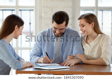 Becoming owners. Happy satisfied young couple husband and wife signing up paper documents, finalizing deal, agreeing to open bank deposit, buying or selling real estate in presence of glad woman agent