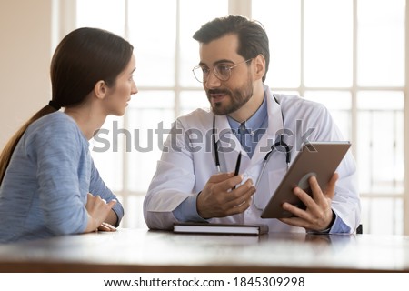 Look at screen, please. Positive capable doc general practitioner demonstrating test results in electronic format or illustrating illness concept to curious patient holding digital tablet pc in hands