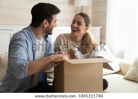 Joyful unboxing. Overjoyed laughing millennial husband and wife new owners renters tenants of house apartment unpacking after relocation moving, happy young spouses receiving awaited postal delivery Royalty-Free Stock Photo #1845311740