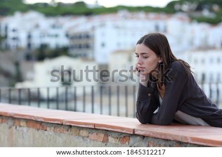 Sad woman complaining alone looking down in a balcony in a town on the beach Royalty-Free Stock Photo #1845312217