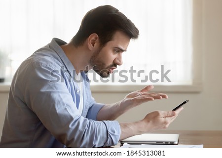 But how... Angry mad shocked millennial male brawling by mobile phone with client support of bank online shop store scolding bad service poor quality of goods purchased slow incorrect application work Royalty-Free Stock Photo #1845313081