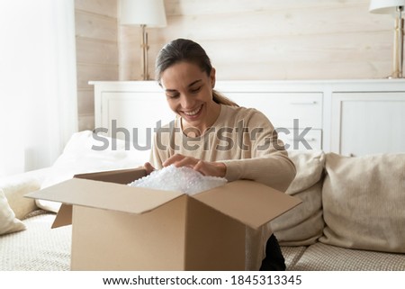 Preparing to relocation. Happy smiling young female buyer tenant renter of new flat packing with love and care at moving day, pleased excited millennial lady receiving unboxing expected postal parcel Royalty-Free Stock Photo #1845313345