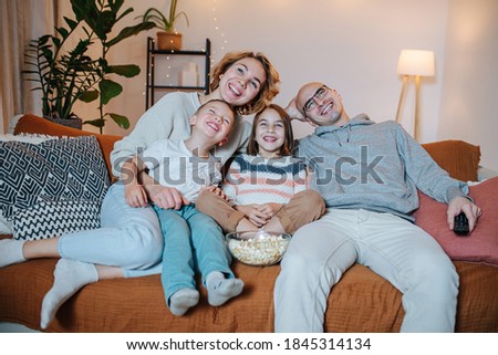 Joyful family of parents and two children watching comedy together on the couch in the living room.
