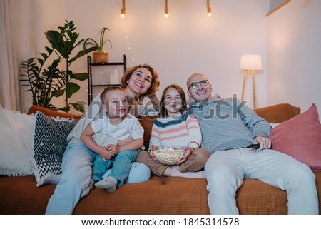 Happy family of parents and two children watching television together on the couch in the living room