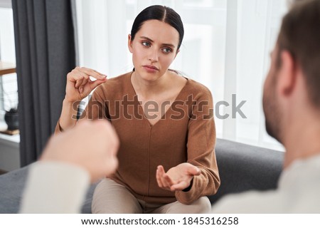 Serious young woman making sign language talk gesturing with her deaf husband at home. Deaf mute woman say no to the man while using nonverbal communication Royalty-Free Stock Photo #1845316258