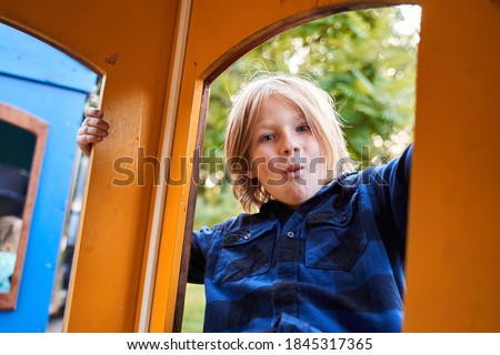 Look at me! Funny little boy wearing plaid shirt looking at the window of kids train at the amusement park. Stock photo