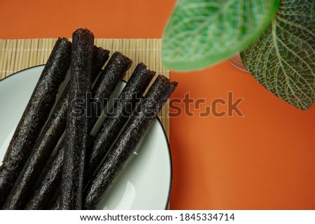 Snacks, seaweed, baked, dried, crispy, on a white round plate, in a bamboo place a plate, orange table top, copy. space, taken from the top corner.