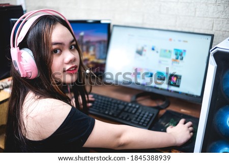 A pretty asian girl wearing a pink headset looks at the camera while doing some online shopping or doing some research on the internet.
