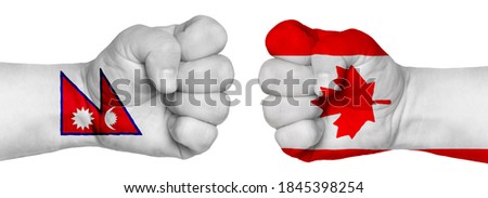 The concept of the struggle of peoples. Two hands are clenched into fists and are located opposite each other. Hands painted in the colors of the flags of the countries. Canada vs Nepal