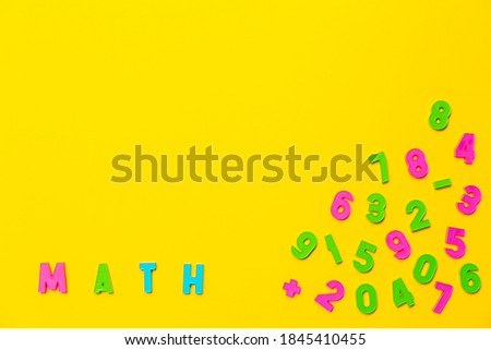 The word math is written on a yellow background in colored plastic toy letters. Nearby are numbers from zero to nine in a chaotic order. Wallpaper for notebooks or school market advertising banner.