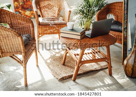 Luxurious and comfortable hotel room in daytime with bamboo chairs and table there are laptop and books with plant on it.