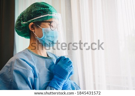 Healthcare worker praying for god blessing while wearing safety equipment for working in hospital during coivd-19 pandemic. Conceptual of woman praying for god to help everythings will be better. Royalty-Free Stock Photo #1845431572